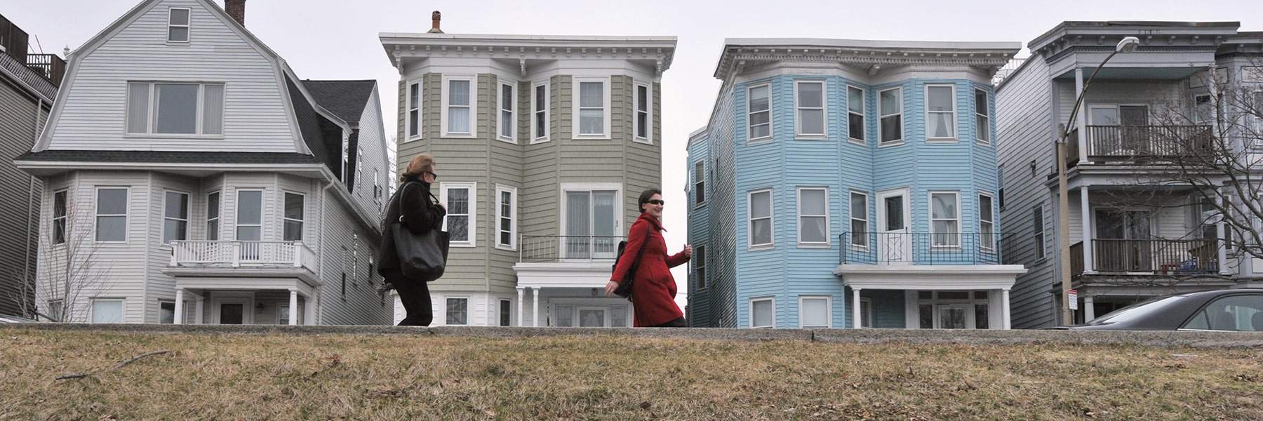 Two people walk past triple decker houses in Dorchester.