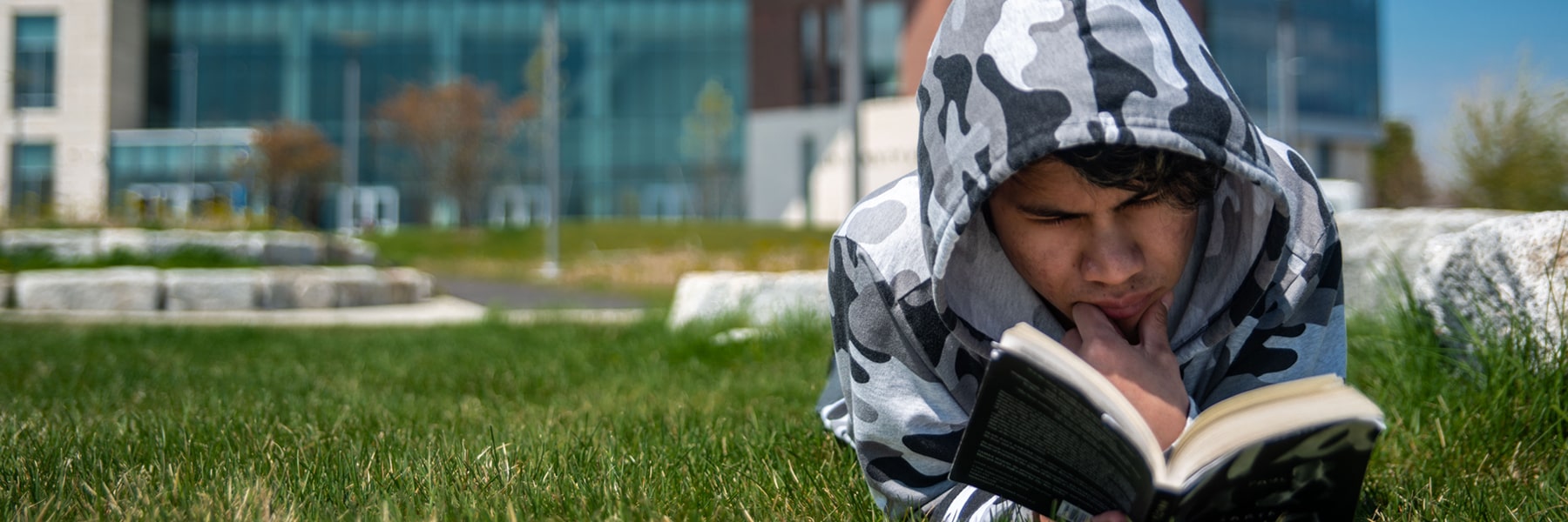 student reads book lying on lawn outside University Hall