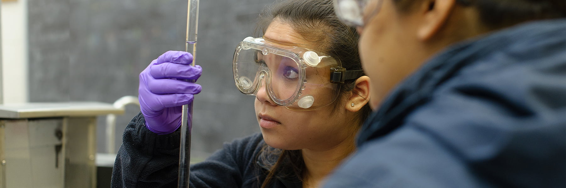 student in goggles holds a test tube.