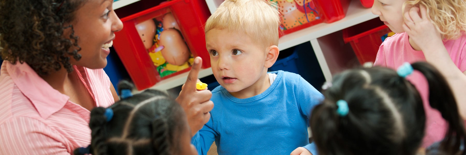 young teacher gesturing to toddlers while holding up index finger