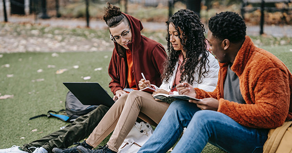 Three students studying together on campus lawn