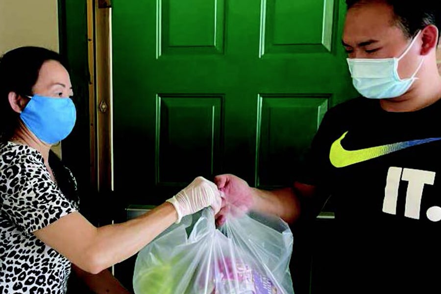 Two asian people wearing masks hold plastic bags of food at a doorway.