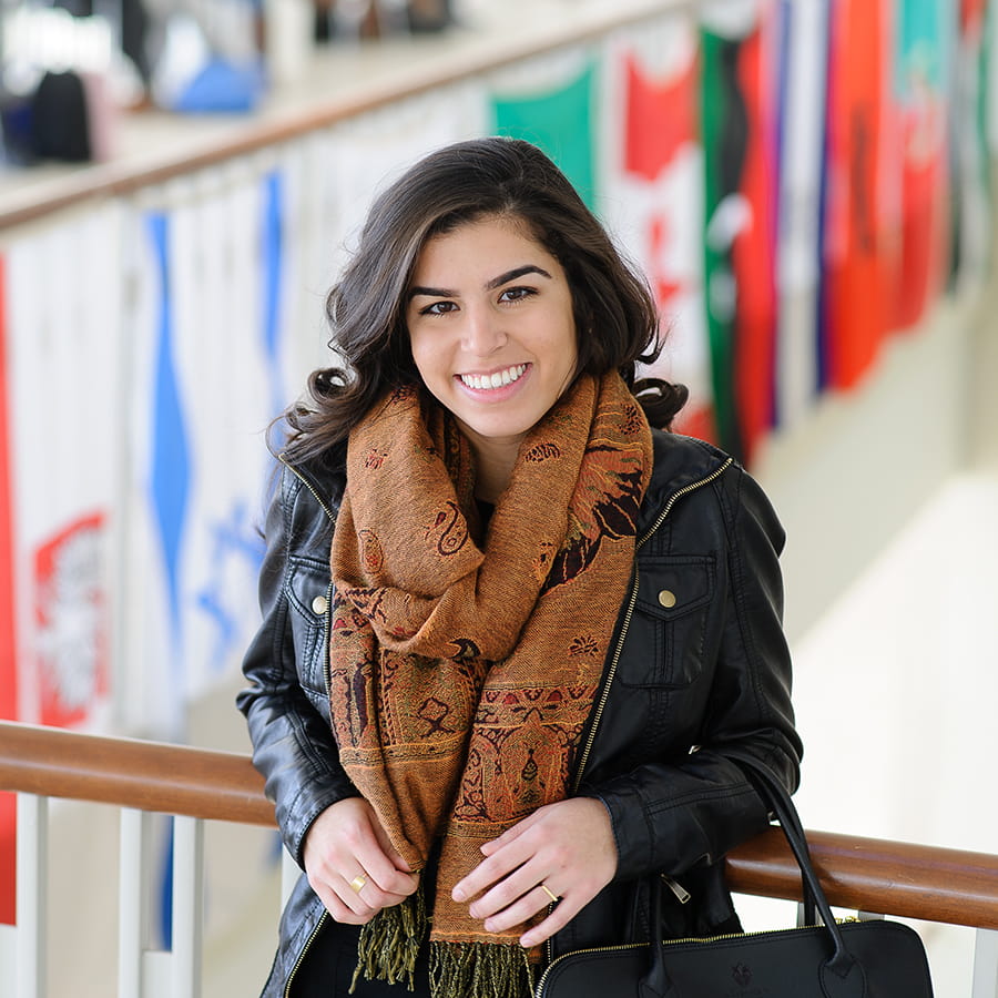 International student stands in front of flags on balcony in Campus Center.