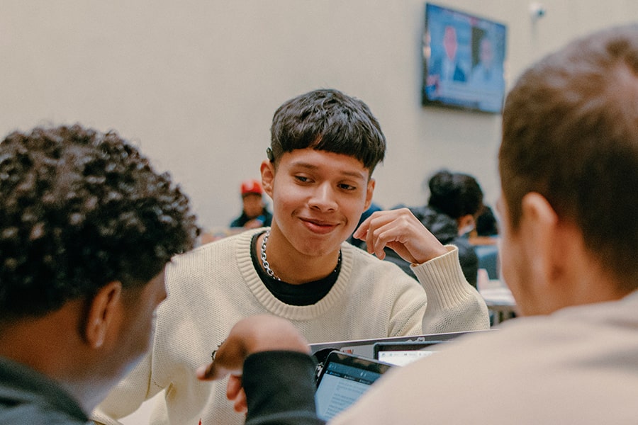 student of color grinning and back of 2 other students facing him
