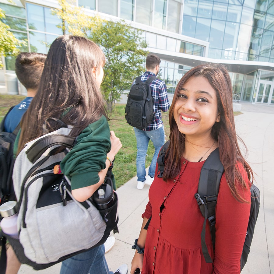 close up of female student in red on sidewalk while students walk nearby