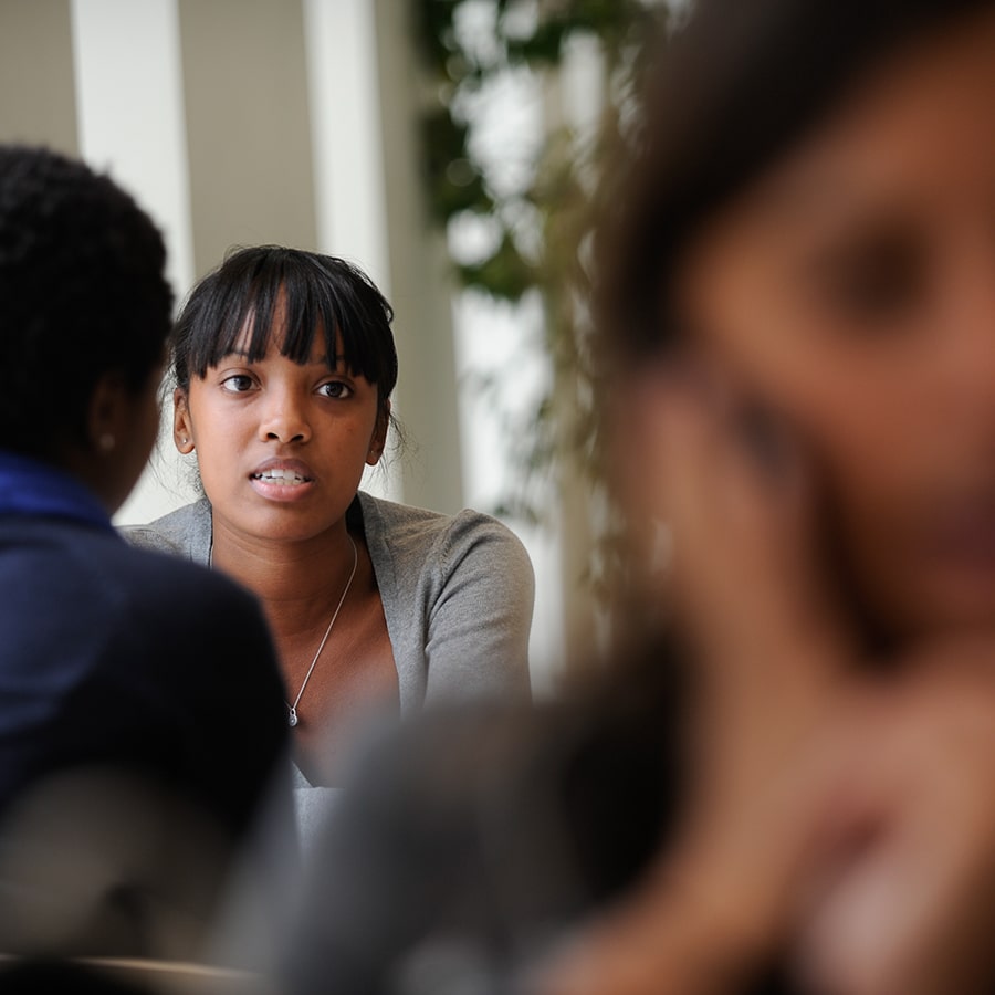 blurred photo of student on phone in foreground with two students talking in background