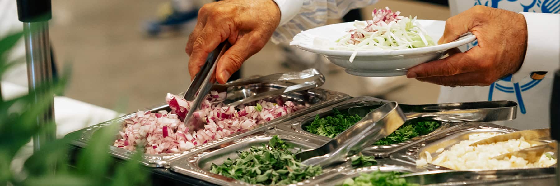 Person using tongs to grab and serve food.