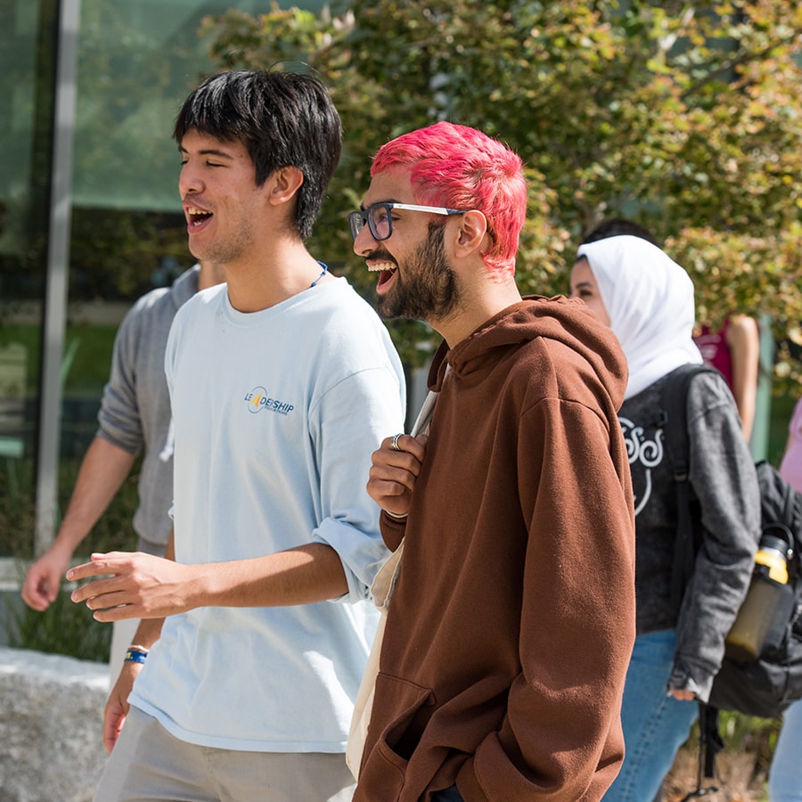 Two students walk on campus one with pink hair