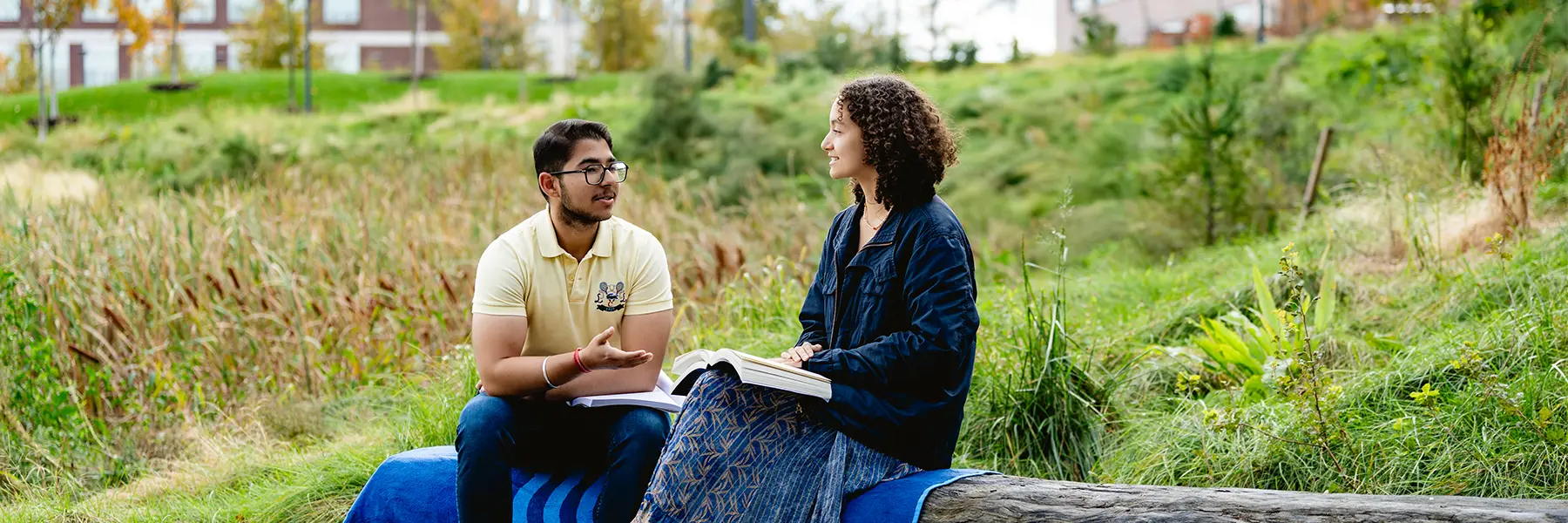 two students study on bench outdoors in quad