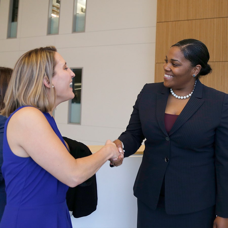 Two female business students shake hands one wears a business suit.