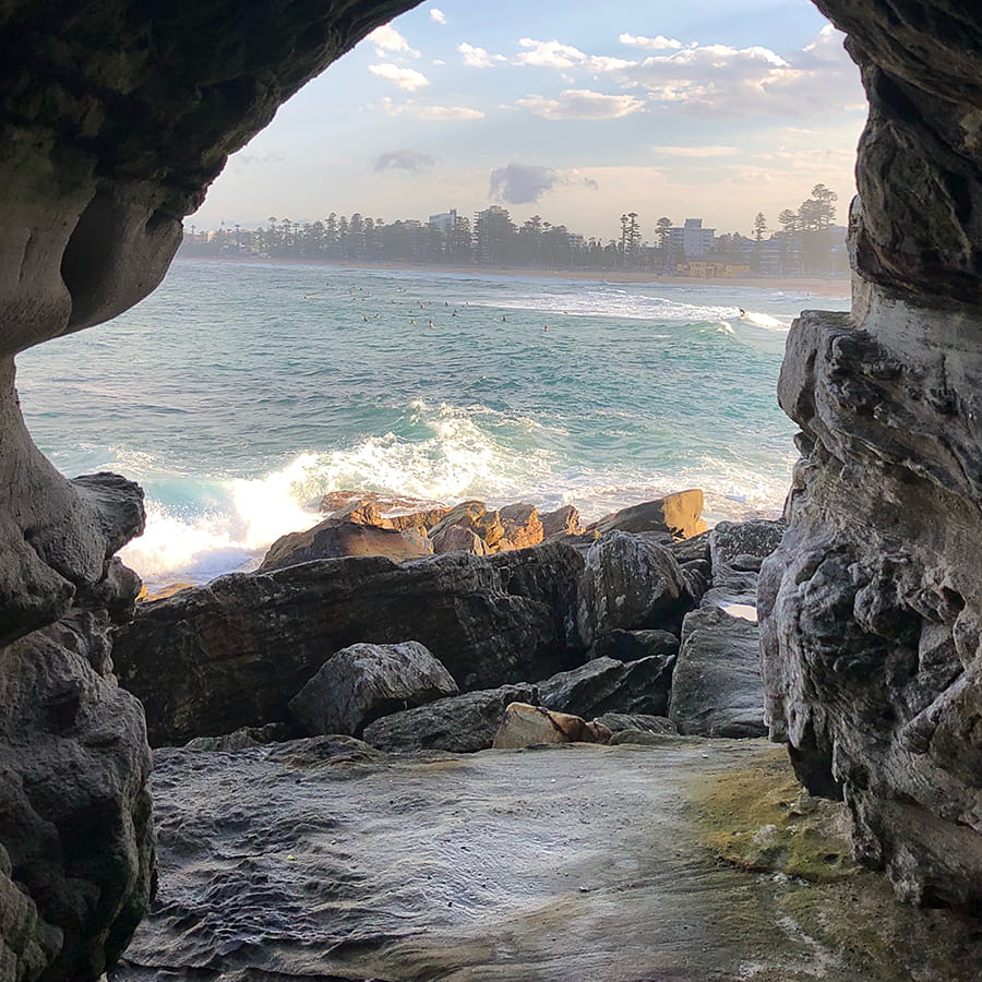 View of Manly Beach through a rock arch with city showing in background in Sydney Australia.