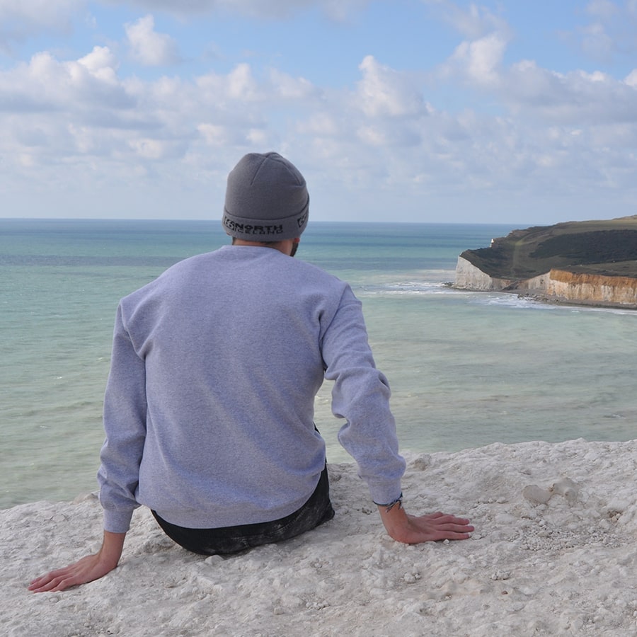 Student sits on beach in long sleeve shirt staring out to sea.