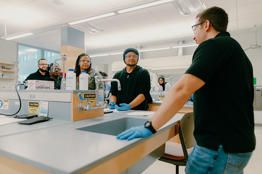 Group of students in the chemistry lab listens to professor.