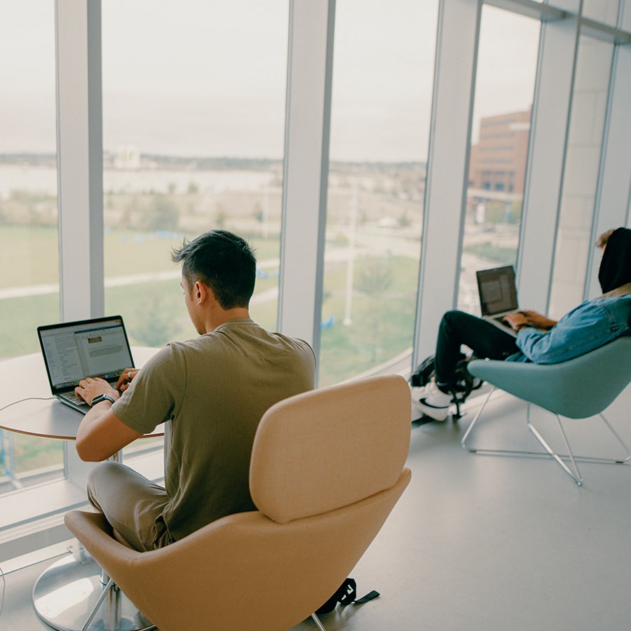 Student on laptop in chair in Uhall balcony facing window.