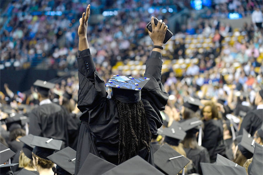 Student raises arms in graduation cap at commencement.