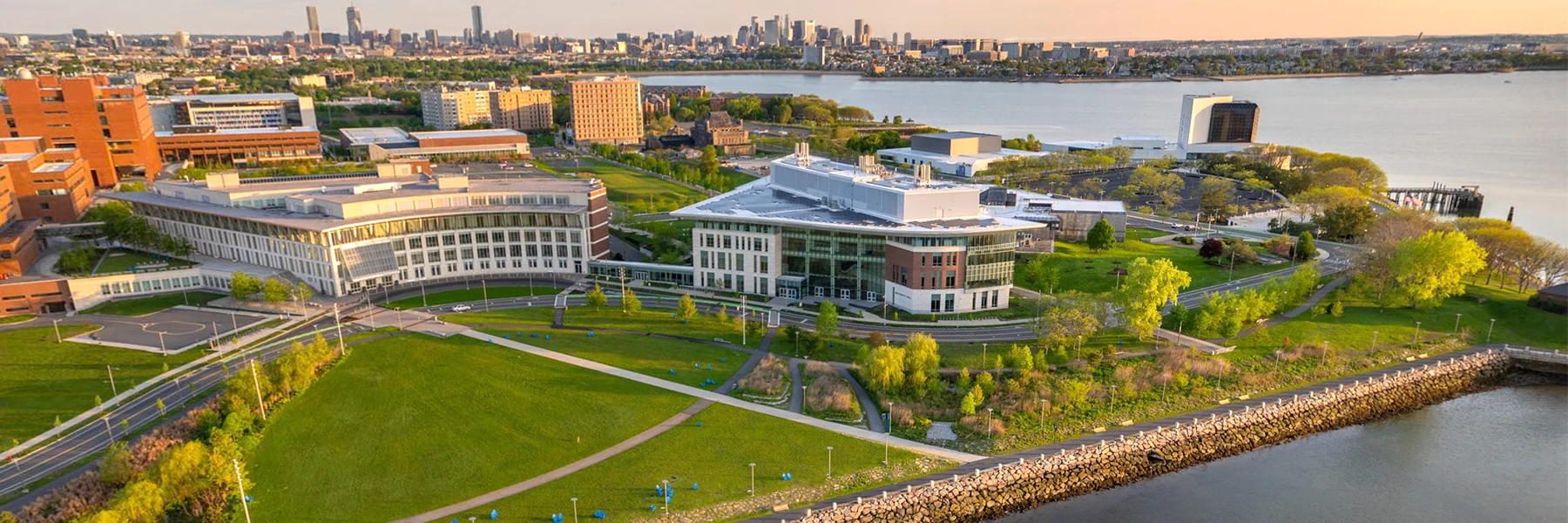 Aerial of UMass Boston campus with harbor and city of Boston skyline in background.