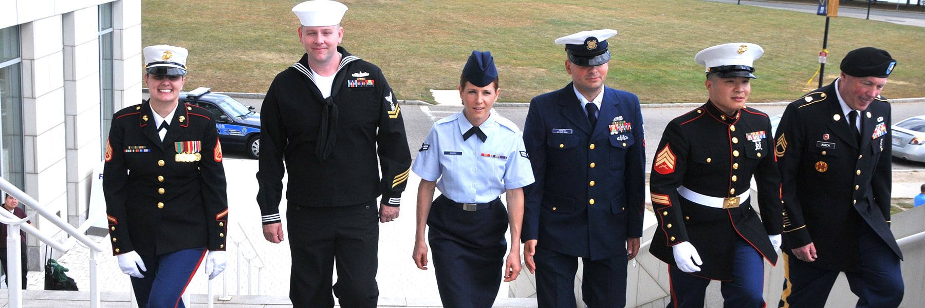 group of veterans in uniform walks up campus center steps.