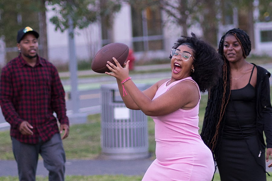 Student in pink dress catches a football.