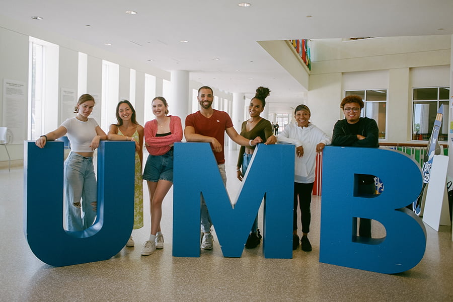 group of students pose by a giant UMB in campus center.