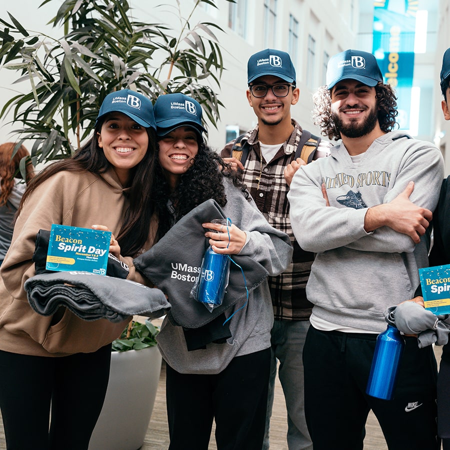 Four students pose in campus center with spirit day swag.