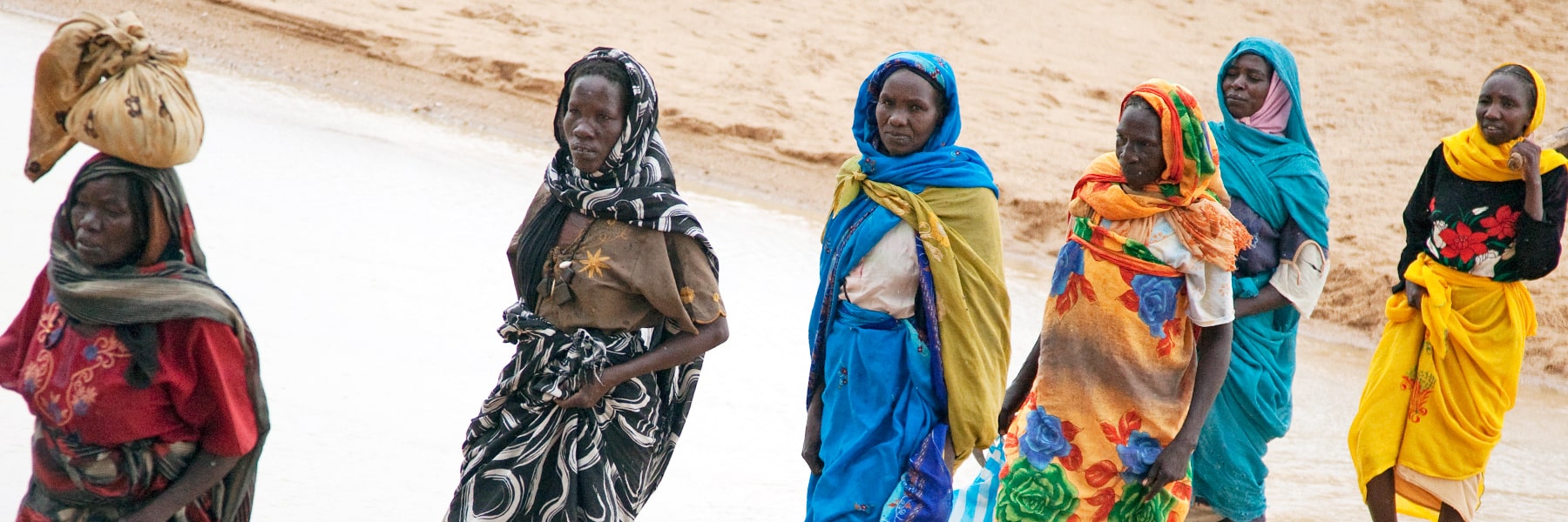 African women walking along desert like background carrying goods on their head