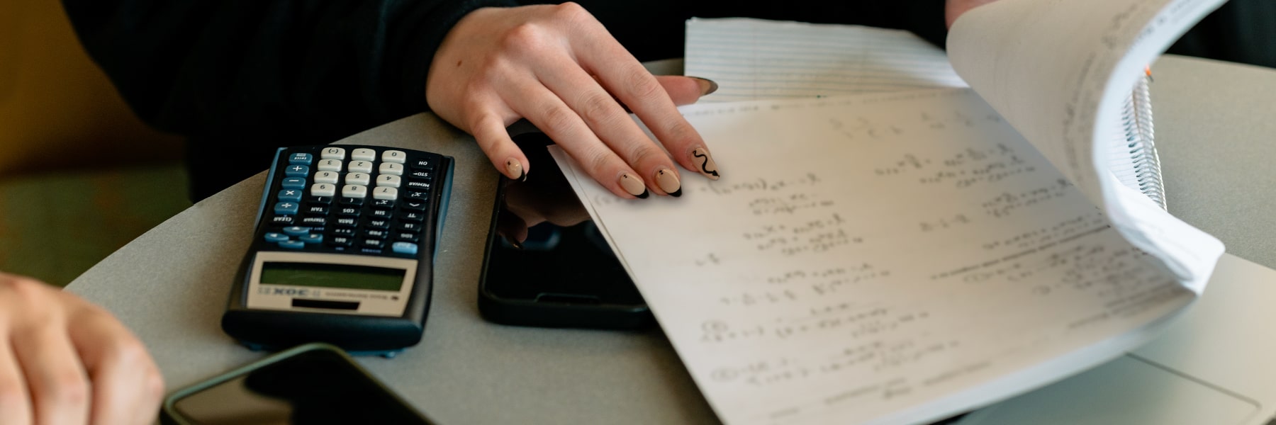 close up of hand with painted fingernails with calculator and notes on paper