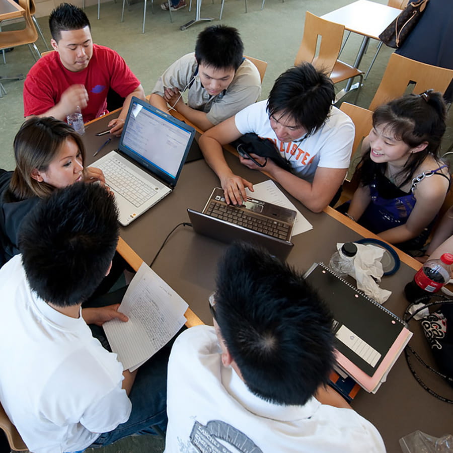 Group of students work on laptops in cafeteria.