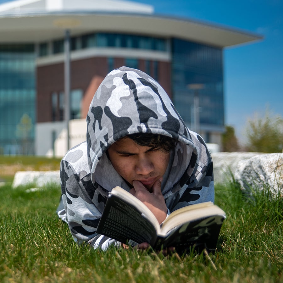 student lying on campus lawn reading a book