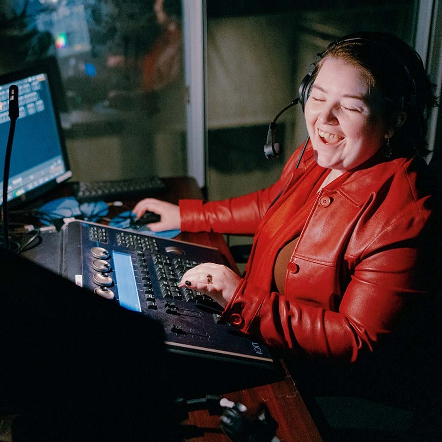 A student smiles while working in an audio production booth wearing a bright red jacket.
