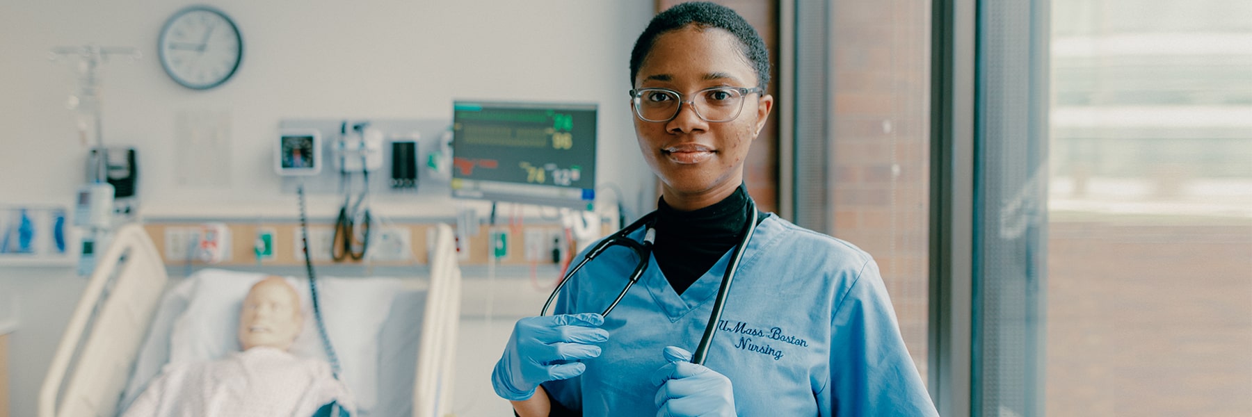 Student nurse in scrubs stands in simulation lab.