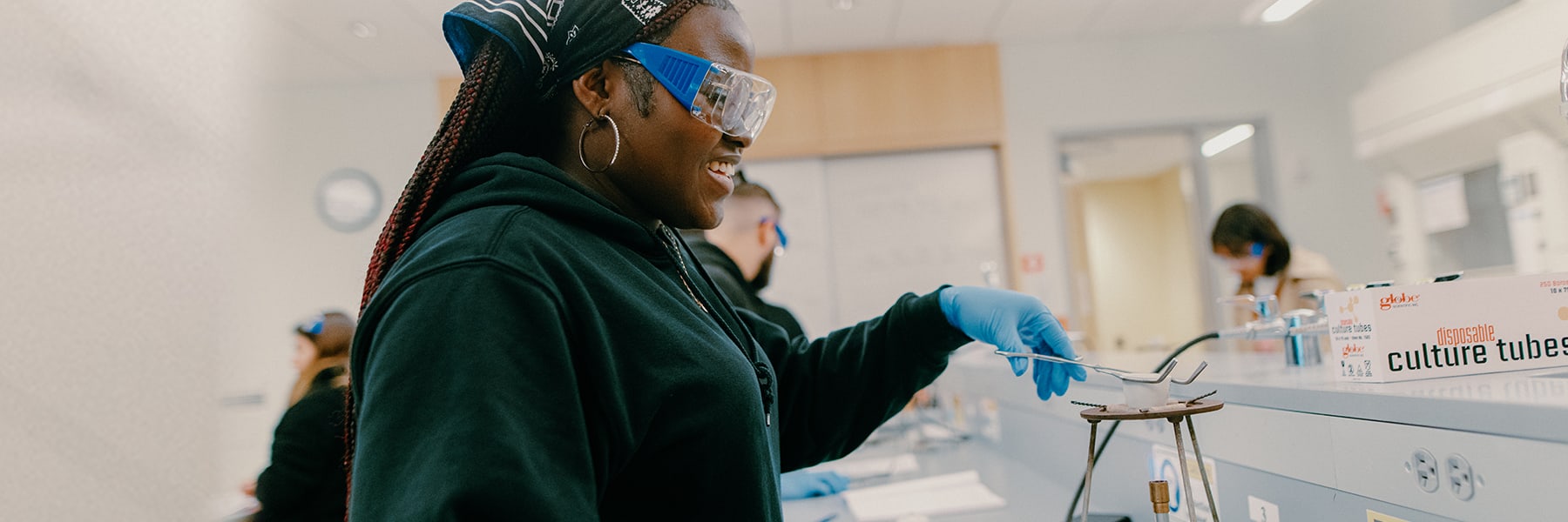 Student in Googles holds equipment at lab station at UMass Boston.