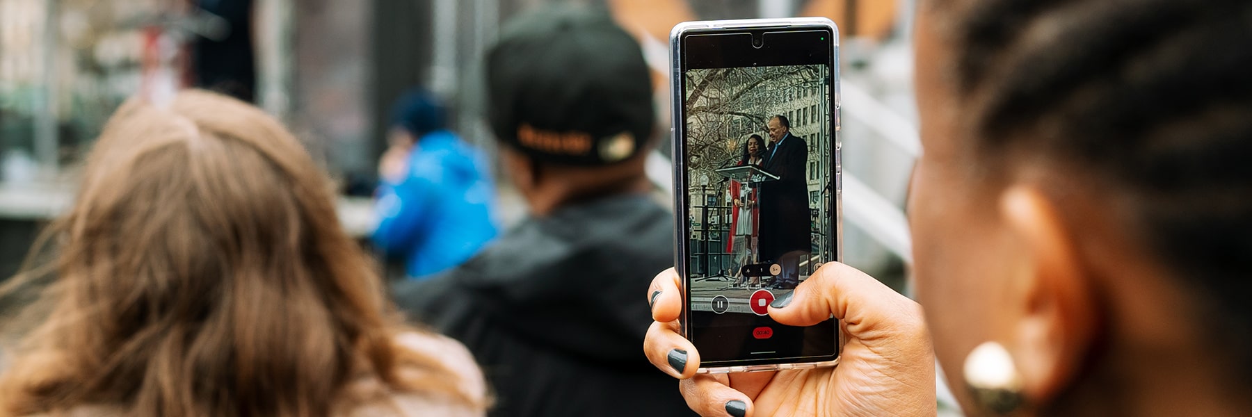 student watches speaker at the Embrace sculpture on cellphone