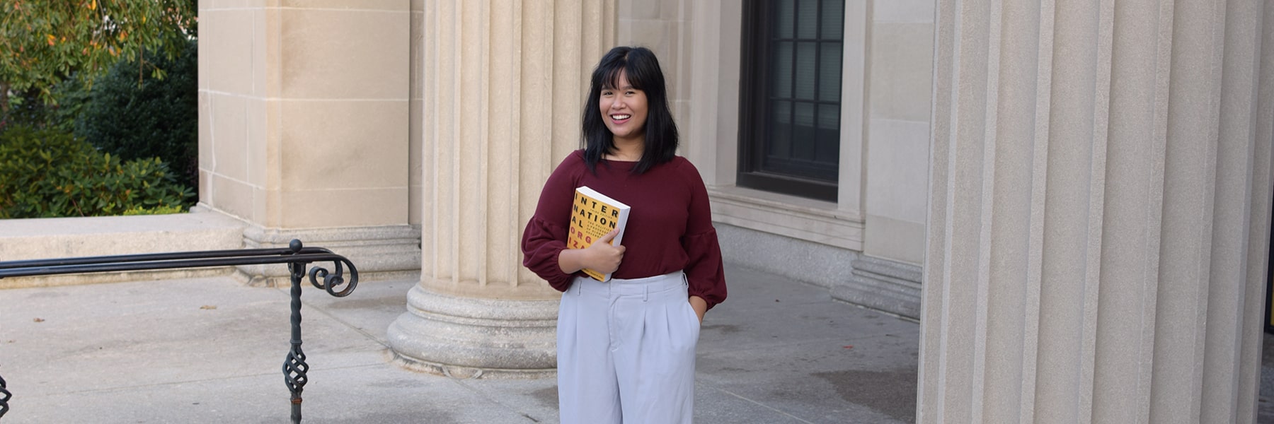 Graduate student in Conflict Resolution holds book on steps of a courthouse.
