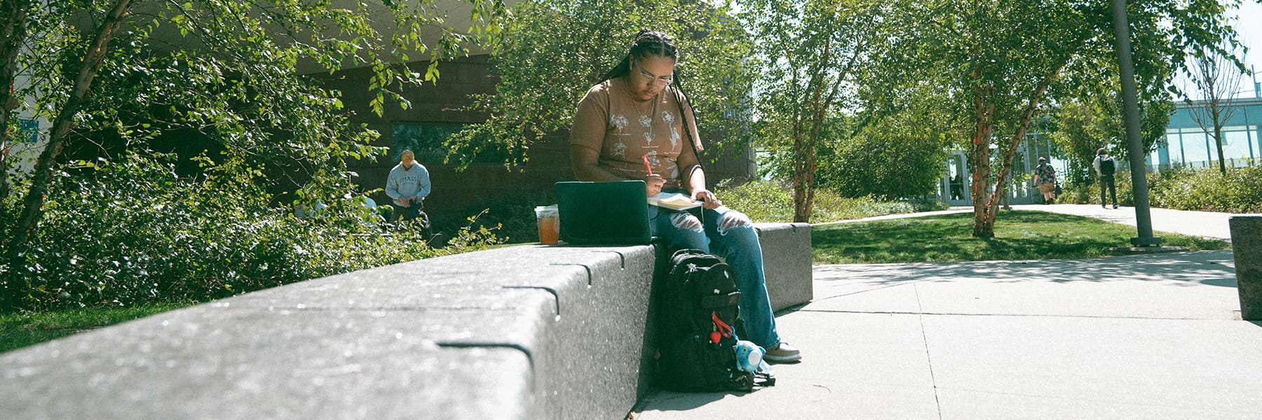 Student does homework outside sitting on a bench on campus.