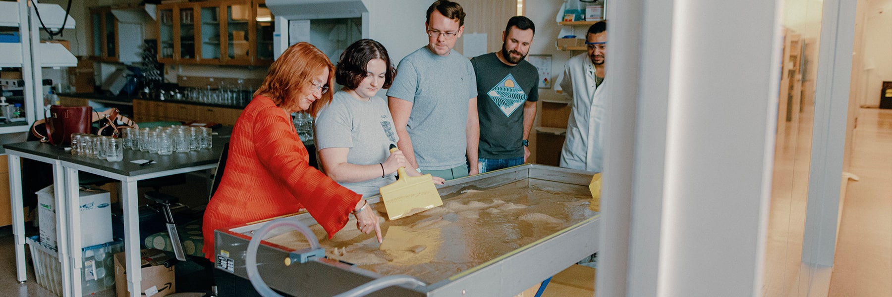 Students work at the wave and sand table in a lab.