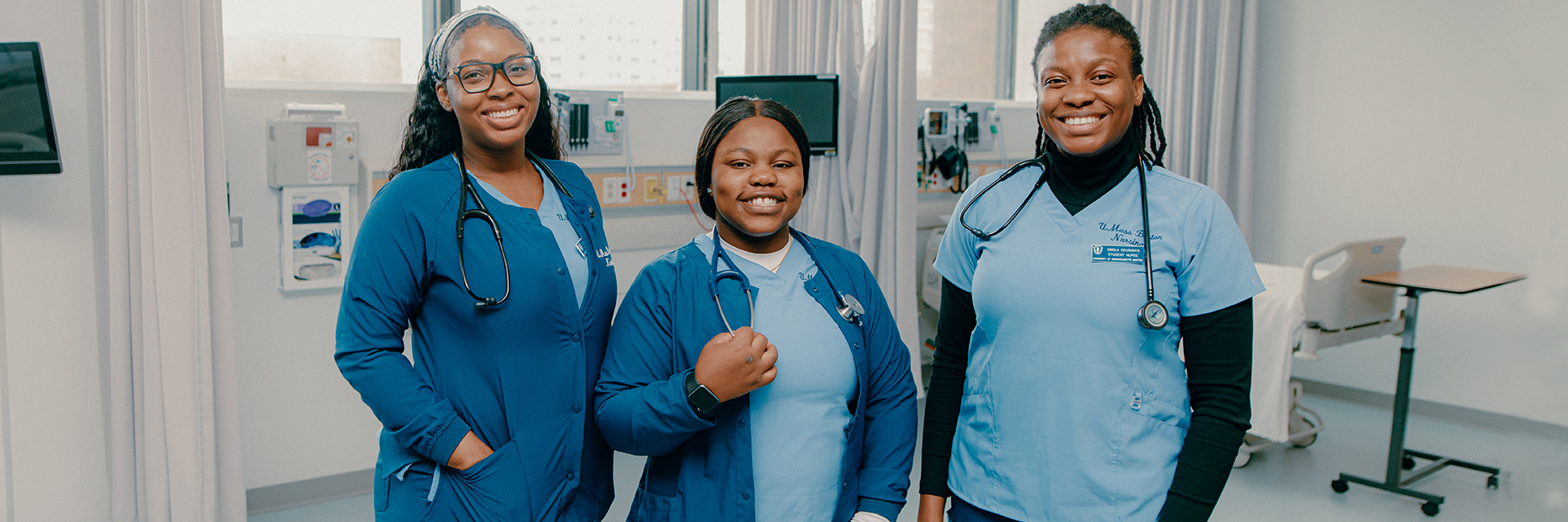 Three nursing students in scrubs stand in simulation lab.