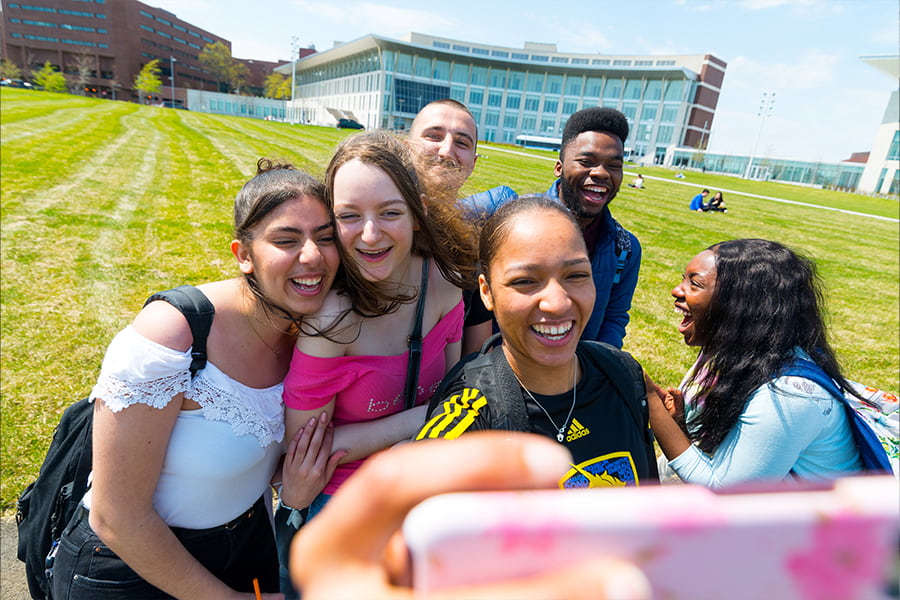 Group of students take a selfie in front of campus center.