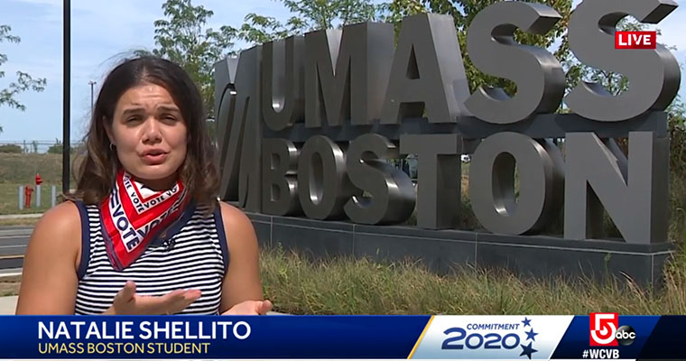 PhD student Natalie Shellito asks candidates a question, while standing in front of the UMass Boston sign on campus.