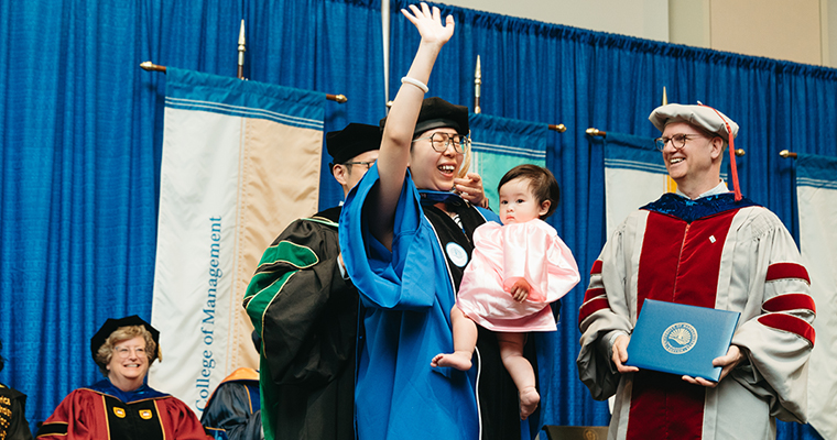 Doctoral candidate is hooded with her child in her arms.