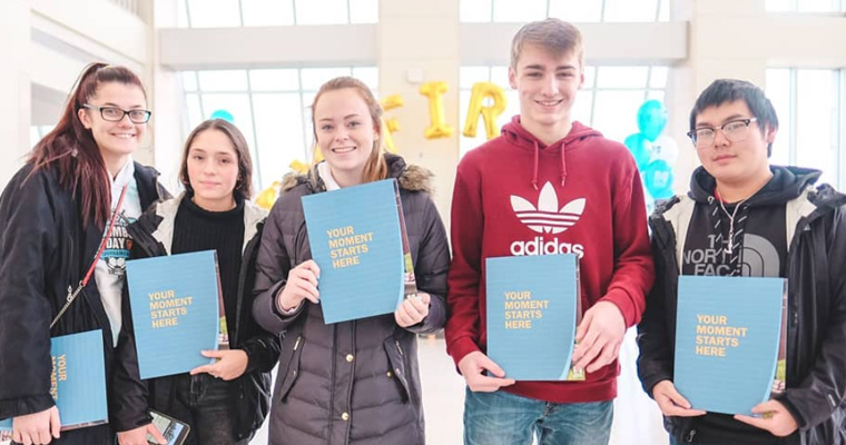 A group of five students holding light blue folders that say, 