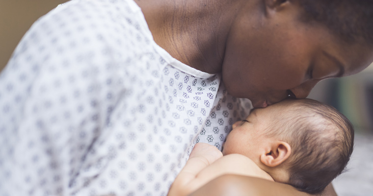 African American mother in a hospital gown kissing newborn 