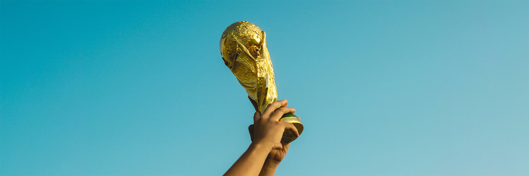 Child holding up FIFA World Cup Trophy in the sky.
