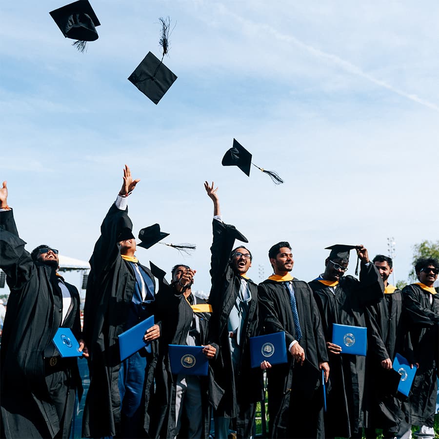 Students in their graduation gowns throwing their caps up into the air.