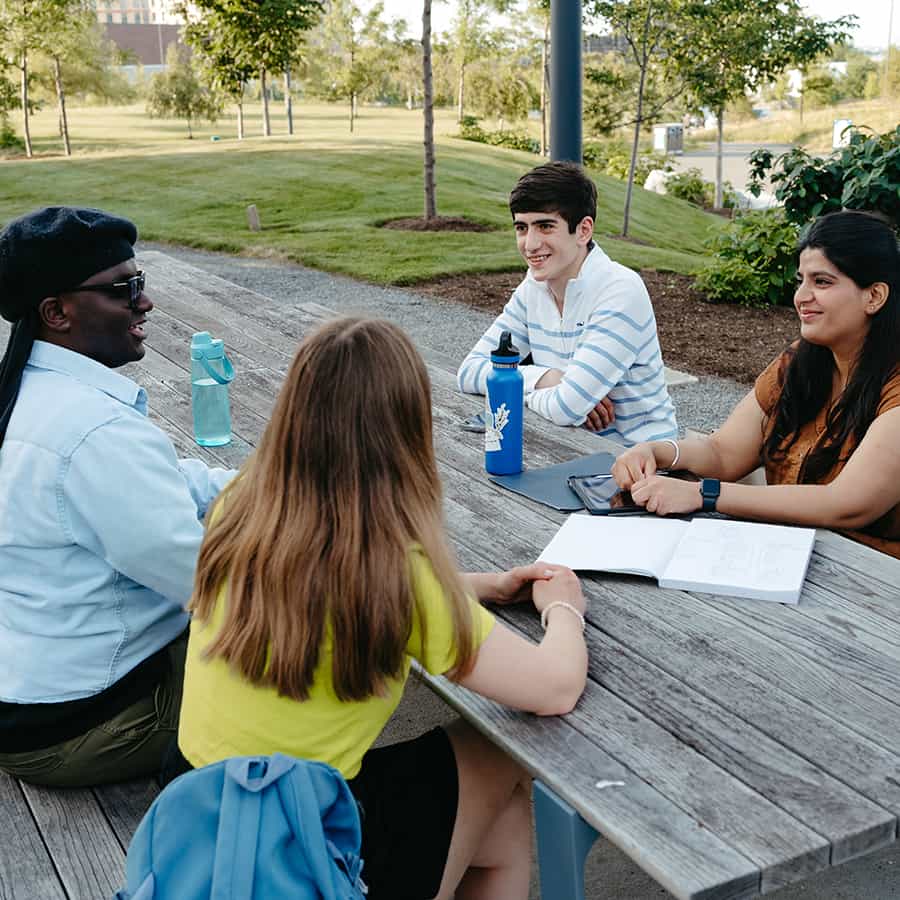 Students sitting at picnic table outside.