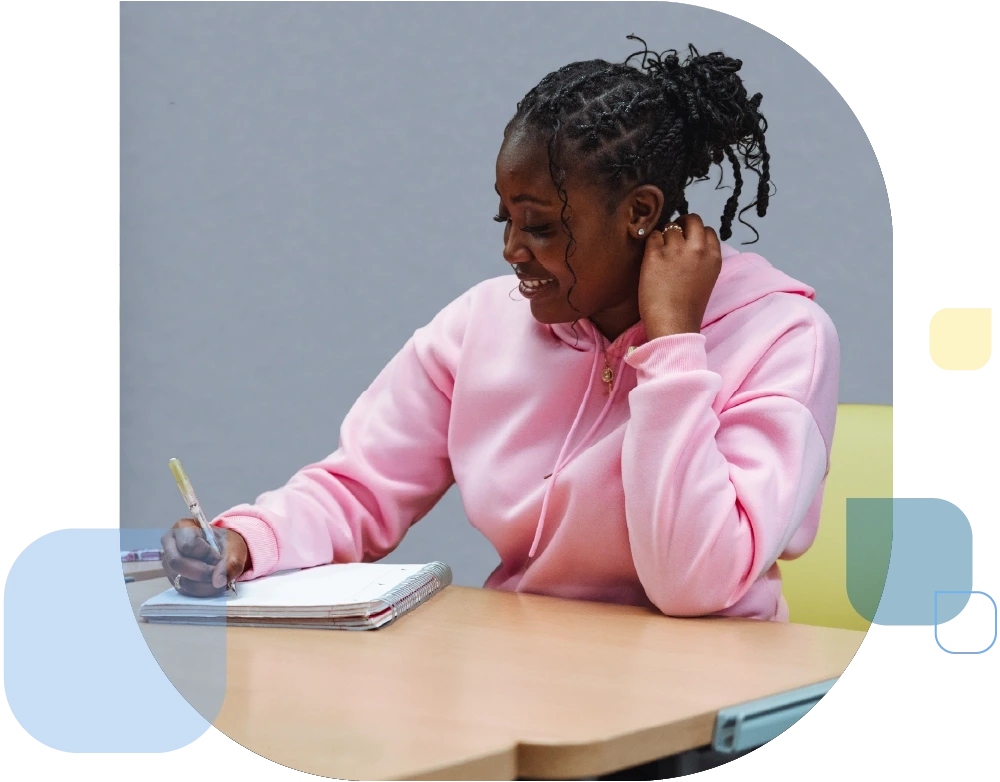 Student wearing pink hoodie writing in her notebook.