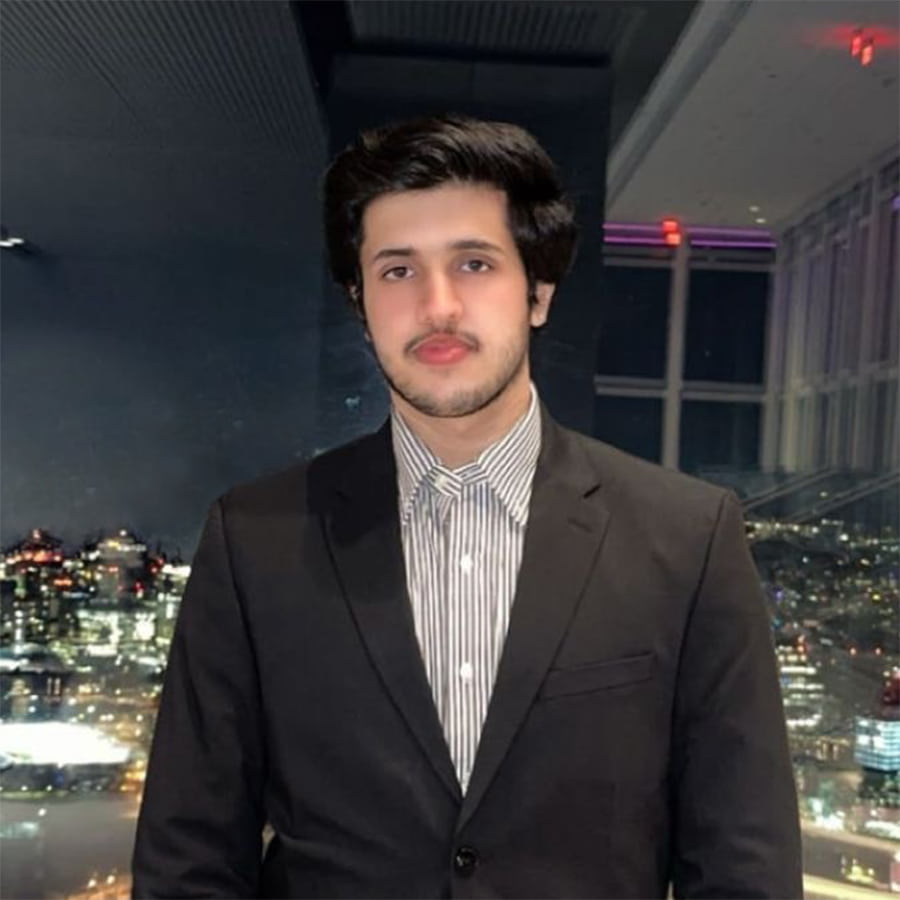 Student, Tanish G., wearing a suit with city skyline in the background.