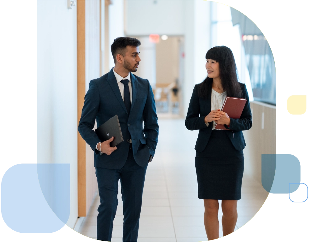 2 students in business attire walking through hall of university with notebooks