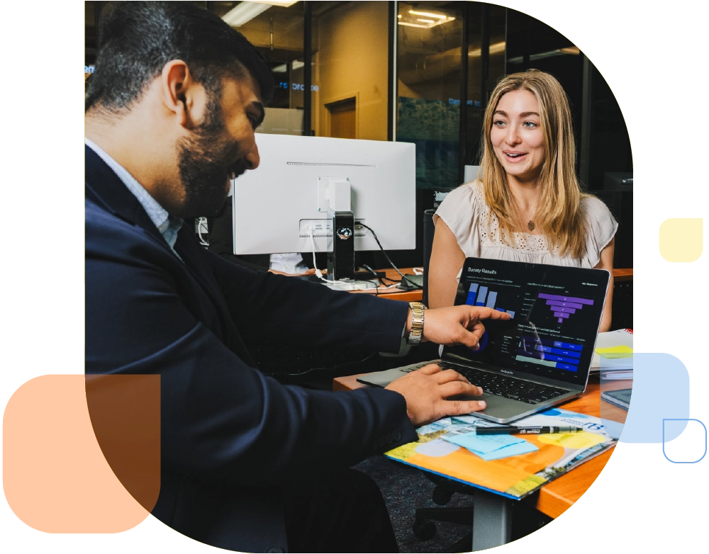 a student in business suit points to a screen in the bloomberg room while another student looks on