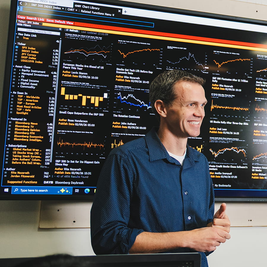 teacher in the Bloomberg Room in front of a screen of stock charts  SP 500 Index