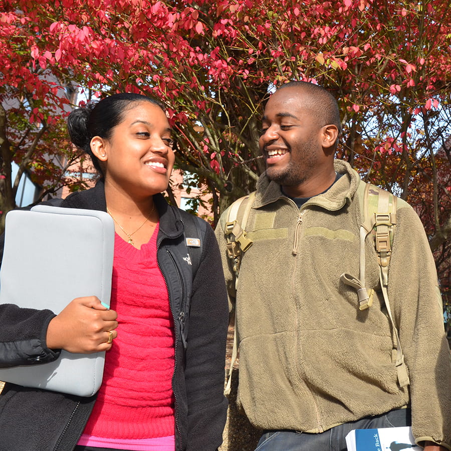 two people outside holding laptop case and book looking at each other in autumn